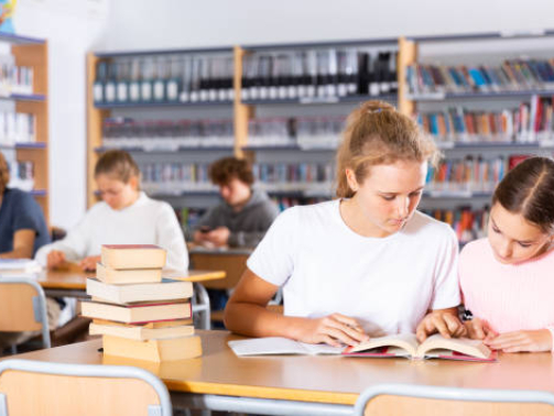 Two female friends reading books together and preparing for exams in the school library