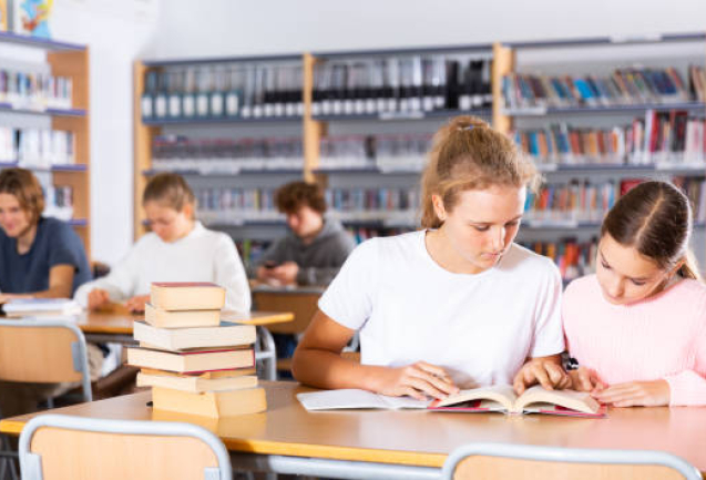 Two female friends reading books together and preparing for exams in the school library