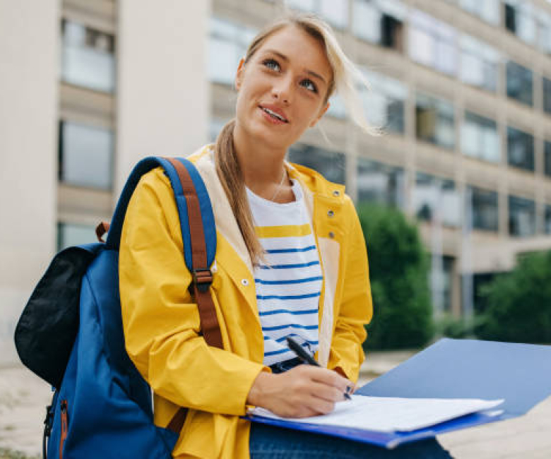 A young Caucasian woman is wearing a bright yellow raincoat and writing on a piece of paper.