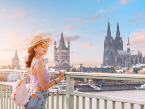 A tourist girl stands on the bridge over the Rhine River and admires the panoramic wonderful view of the Cologne Cathedral and cityscape