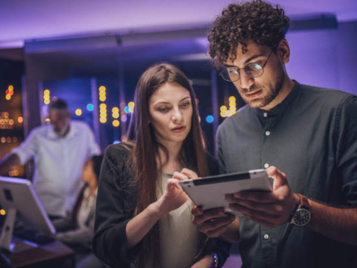 Male and female maintenance engineers examining data on digital tablet together in server room.